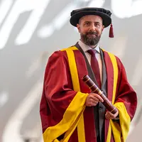 A man in a graduation robe and cap proudly holds his diploma, celebrating his academic achievement.