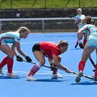 Women engaged in a field hockey match on a bright blue field, demonstrating skill and collaboration in the sport.
