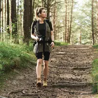 A woman walking through a forest. She is wearing walking gear and carrying a camera.