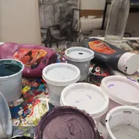 A collect of opened and used paint cans sit on a cluttered table filled with art supplies
