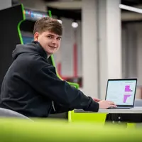 A young man works on a laptop at a table in an open workspace.