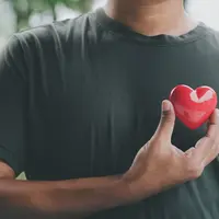 A man holding a small red heart against his chest.