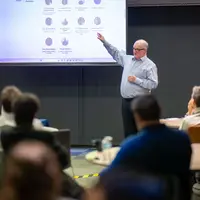 A member of the Centre for International Research in Interactive Technologies for Teaching and Learning staff points to the audience during a presentation
