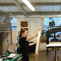 An individual working on a large sheet of paper, in a art room class setting.