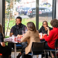 A group of people are sitting around a table. A banner with DARPL on it is visible in the background.