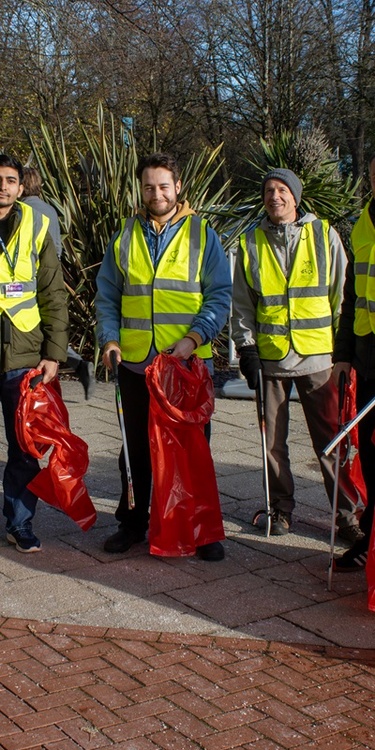 A group of litter pickers in high visibility vests hold waste bags and litter picking sticks