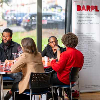 A group of people are sitting around a table. A banner with DARPL on it is visible in the background.