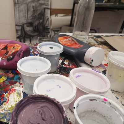 A collect of opened and used paint cans sit on a cluttered table filled with art supplies