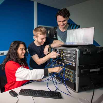 Three students work together, connecting cables to a network switch.