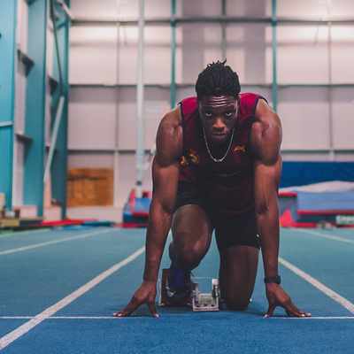An athlete crouches in a starting position on a blue indoor track, preparing to sprint.