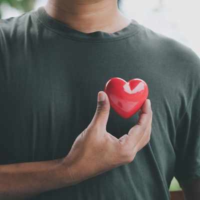 A man holding a small red heart against his chest.