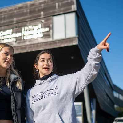 A Student Ambassador giving directions to an Open Day visitor outside the Cardiff School of Management building.
