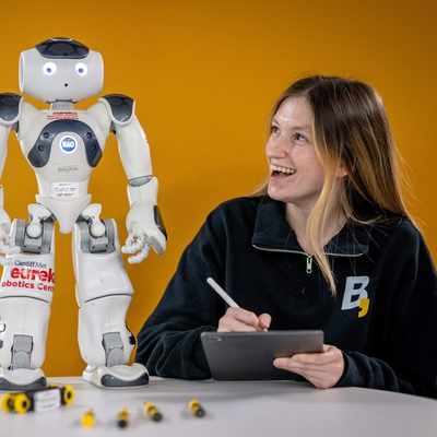 Person holding a tablet and stylus while looking up at a small humanoid robot.