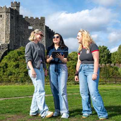 Three people stand together in front of a large, historic castle keep.