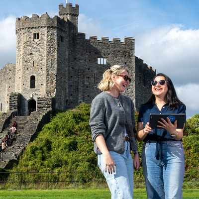 Two people stand together in front of a large, historic castle keep.