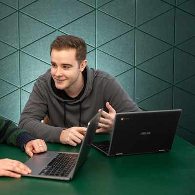 Two individuals seated at a table, each using a laptop, engaged in a collaborative work session.