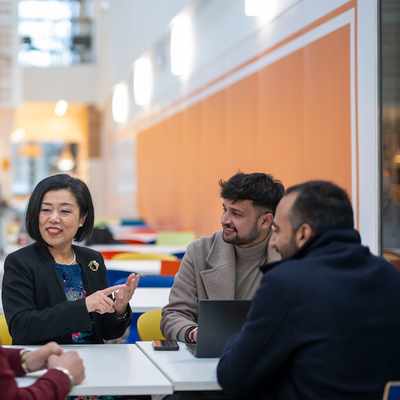 A person in a black blazer stands smiling in front of a modern building with Cardiff Metropolitan University signage. The sky is clear.
