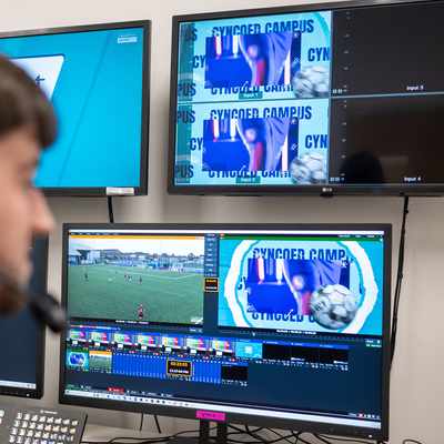 A person in headphones watches a football match on several monitors.
