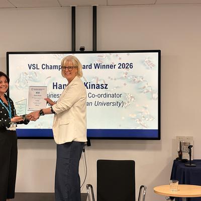 Hannah Kinasz recieving an award from a collegue in front of large monitor
