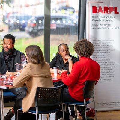 A group of people are sitting around a table. A banner with DARPL on it is visible in the background.