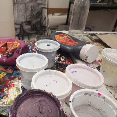 A collect of opened and used paint cans sit on a cluttered table filled with art supplies