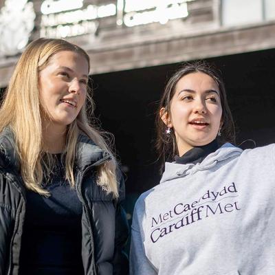 A Student Ambassador giving directions to an Open Day visitor outside the Cardiff School of Management building.