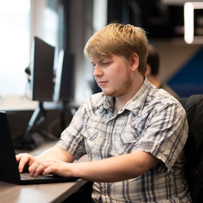 A young man in a short sleeve pattern shirt types on a laptop at a desk