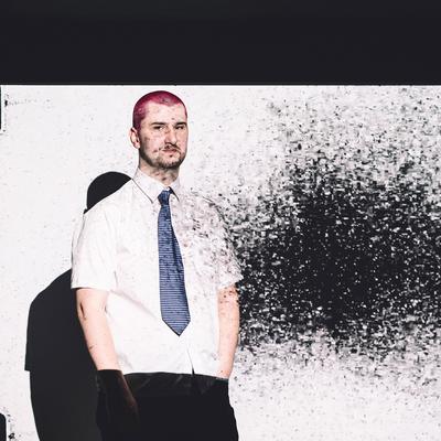 A man with pink hair stands in front of a large screen, engaging with the displayed content.