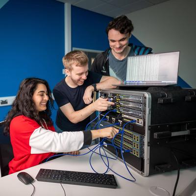 Three students work together, connecting cables to a network switch.