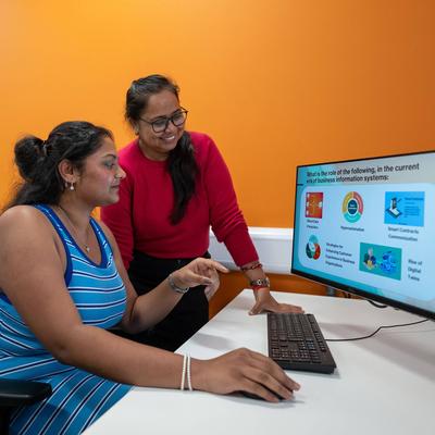Two people collaborating in front of a computer screen, engaged in discussion and reviewing information together.