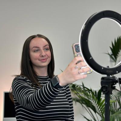 A person filming themselves using a mobile, illuminated by a ring light.