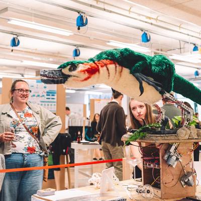 A group of people view a mechanical model of a prehistoric bird. The bird is standing on a pedestal with motors and wires visible beneath.