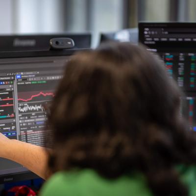 A person points to a large computer monitor showing financial charts.