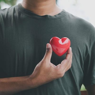 A man holding a small red heart against his chest.