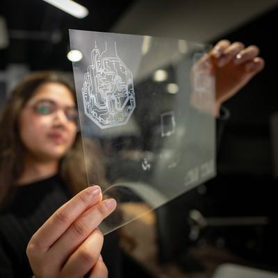 A person holds a small transparent sheet, etched with electronic circuits.