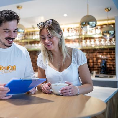 Aerial view of a vibrant waterfront city with winding rivers, numerous buildings, and a marina. The landscape features green spaces and urban areas under a clear blue sky.