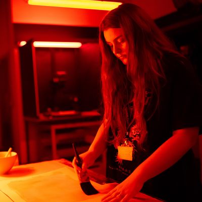 Two people in a photography studio look at a cameras screen, smiling. They stand close together, with lighting equipment visible in the background. One person wears a green cap and holds the camera.