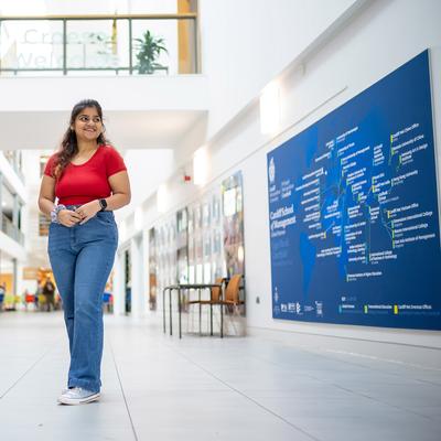 A man in a white shirt stands with his hands on a railing, smiling broadly in a modern, multi-story building with glass windows and wooden accents.