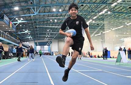 School pupil running with rugby ball on the running track inside the National Indoor Athletics Centre at Cardiff Metropolitan University's Cyncoed campus