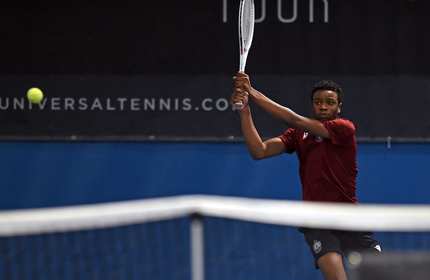 A young man swings a tennis racket at the ball with both hands