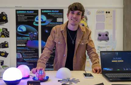 A man is positioned before a laptop and a lamp, engaged in his tasks in a bright setting.