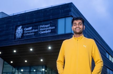 Kush Shinde stands with arms in their jacket pockets outside the Cardiff School of Managament