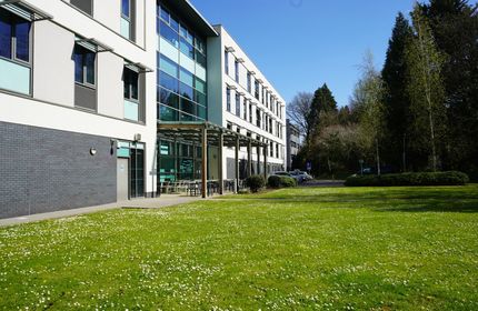 Rear view of the Cardiff School of Management, including an open green space and outdoor seating, on a sunny day