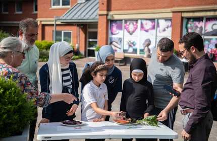 A group of people varying in age stand around a table inspecting vegetables