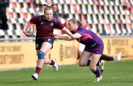 A Cardiff Met player runs with a rugby ball while holding off an opponent with their arm during a rugby match
