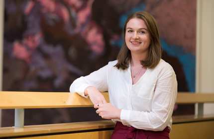 A young woman in a white blouse leans with one arm on a wooden railing.