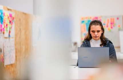 A young adult works from a laptop in an arts workspace.