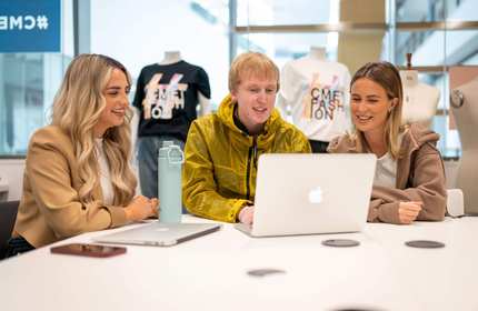 Three people sit alongside each other at a table with laptop computers.