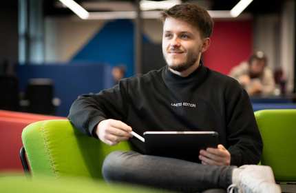 A person sits on a couch with a tablet computer resting on their knee.