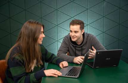 Two students with laptops in conversation